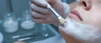 Professional microneedling facial treatment with derma pen device on woman's face with white cream mask in modern spa clinic setting.