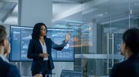 Professional African American businesswoman presenting financial data analytics on digital screen in modern corporate boardroom meeting.