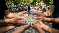 Diverse group of people joining hands together holding colorful badges in circle formation outdoors, symbolizing unity, teamwork, community support and collective collaboration at public event.