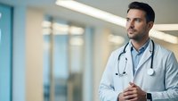 Professional male doctor with stethoscope in modern hospital corridor looking confidently ahead for healthcare and medical consultation concepts.
