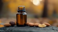 Amber glass essential oil bottle with almonds on stone surface in warm natural lighting for aromatherapy and wellness products.
