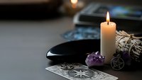 Mystical altar setup with burning candle, amethyst crystal, sage bundle, pentagram symbol and tarot cards for spiritual rituals and divination practices.