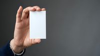 Close-up of male hand holding blank white card against gray background, isolated for business branding, marketing mockups, and corporate design projects.