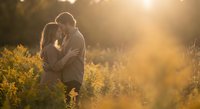 Young couple embracing in golden sunlight field during romantic sunset moment with warm lens flare and natural outdoor lighting for love and relationship concepts.