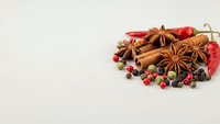 Aromatic spices collection with star anise, cinnamon sticks, dried chili peppers and colorful peppercorns arranged on neutral background for culinary designs.