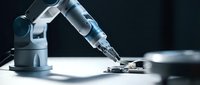 Industrial robotic arm performing precision assembly work on electronic components in modern manufacturing facility with dramatic lighting.