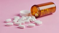 Prescription medication pills spilled from amber pharmacy bottle on pink background for healthcare and medical treatment concepts.