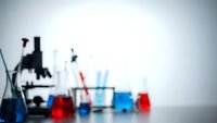 Laboratory equipment with microscope and colorful chemical solutions in glass beakers creating scientific research atmosphere for educational content.