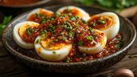 Halved boiled eggs topped with spicy chili sauce and fresh chopped herbs served on rustic ceramic plate, close up view of Asian fusion appetizer on wooden table.