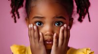 Young African American girl with surprised expression holding hands on cheeks, wearing yellow dress against pink background, showing genuine emotion and innocence.