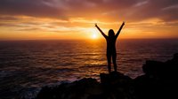 Woman silhouette with raised arms celebrating success at ocean sunset from rocky cliff with golden sky and waves below for motivation concepts.