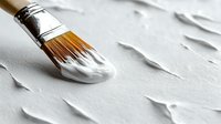 Paint brush with white paint on textured surface creates minimalist artistic composition showing brush strokes and creative process in soft natural lighting.