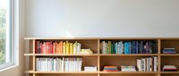 Organized wooden bookshelf with colorful books arranged by color spectrum creating rainbow effect in modern minimalist home library interior.