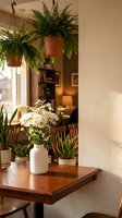 Cozy indoor plant corner with hanging ferns, white flowers in ceramic vase and succulents on wooden table creating warm home atmosphere for interior design.