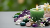 Green candle burning surrounded by healing crystals, gemstones and white flowers creating peaceful spa atmosphere for meditation and wellness rituals.