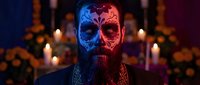 Day of the Dead celebration with painted skull face man surrounded by candles and marigold flowers in atmospheric lighting for Halloween and cultural festivities.