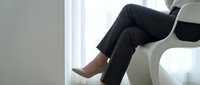 Professional businesswoman in black suit sitting in modern white chair by window in minimalist office interior for corporate and workplace concepts.