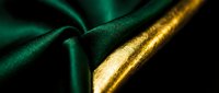 Luxurious emerald green fabric with gold trim detail on dark background, suitable for fashion, textile, and luxury design projects.