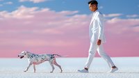 Young Asian man in white suit walking Dalmatian dog on minimalist white surface against pink sunset sky with clouds, surreal artistic composition.