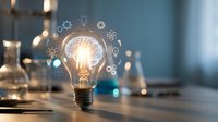 Glowing light bulb with innovation icons and gears floating around it on modern desk. Creative thinking, brainstorming and business solution concept.