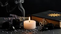 Mystical witchcraft altar with burning candle, lavender herbs, pentagram pendant, spell book and scattered seeds creating atmospheric spiritual scene.