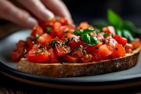 Fresh bruschetta with diced tomatoes and basil on toasted bread being garnished by hand, appetizer preparation for Italian cuisine and cooking concepts.