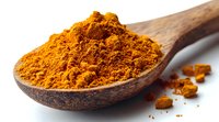 Ground turmeric powder in wooden spoon on white background, bright orange spice with scattered particles, close up macro shot showing texture and vibrant color.