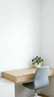 Minimalist home office workspace with wooden floating desk, gray upholstered chair and small potted plant against clean white wall for modern interior design.