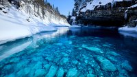 Crystal clear turquoise hot spring pool surrounded by snow-covered rocks and evergreen trees in winter mountain landscape for travel and nature themes.