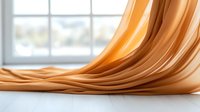 Flowing golden fabric creates smooth waves and folds against white background, soft focus window light adds depth and dimension to luxurious textile surface.