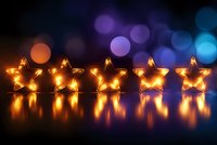 Glowing star-shaped lights arranged in row with warm yellow illumination reflecting on surface against blurred bokeh background in purple and blue tones.