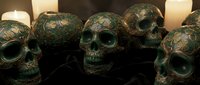 Ornate bronze skulls with intricate floral patterns arranged in a group, illuminated by candlelight for gothic, Halloween, or dark fantasy design projects.