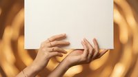 Female hands holding blank white paper sheet against golden bokeh background for mockup design and branding presentations.