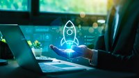 Businessman in suit holding glowing rocket hologram above hand, digital dashboard in background, symbolizing startup launch and innovation.