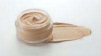 Open glass jar with beige foundation cream and makeup smear on white background. Cosmetic product for skincare and beauty routine isolated.