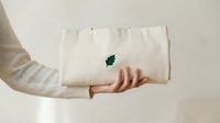 Caucasian woman holding a natural cotton tote bag with a small green leaf embroidery, eco-friendly sustainable fashion accessory on light background.