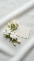 White jasmine flowers with buds arranged beside blank cream card on neutral linen fabric with soft shadow, suitable for wedding invitations and stationery design.