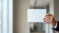 Businessman holding blank white card in office environment with blurred background, suitable for business messaging and corporate communications.