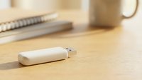White USB flash drive on wooden desk with notebook and coffee mug in background for office technology and data storage concepts.
