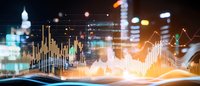 Financial data visualization with glowing charts and graphs overlaid on blurred city skyline at night, showing market trends and analytics.