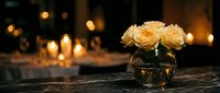 Elegant cream roses in glass vase on marble surface with warm candlelight bokeh background creating romantic dining atmosphere for special occasions.