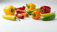 Assorted fresh bell peppers and chili peppers in vibrant yellow, red, orange, and green colors arranged on white background for culinary and food styling projects.
