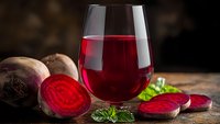 Fresh beetroot juice in glass with sliced raw beets and herbs on wooden table. Healthy detox drink rich in vitamins and antioxidants for wellness lifestyle.