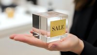 Businesswoman holding transparent glass cube with golden sale label in palm, retail marketing concept for promotional campaigns and discount offers.