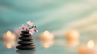Zen spa stones balanced with delicate cherry blossoms against soft bokeh lights creating peaceful meditation atmosphere for wellness relaxation.