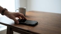 Man's hand reaching for smartphone on wooden desk with coffee mug, workspace communication and technology concept for business, office, and digital connectivity themes.