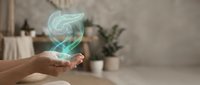 Hand holding glowing green holographic heart symbol in modern home interior representing healthcare technology and digital wellness concepts.