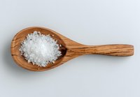 Sea salt crystals on wooden spoon against neutral background, highlighting natural texture and culinary ingredient for gourmet cooking.