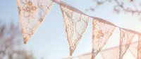 Delicate lace bunting flags hanging outdoors in soft natural light creating romantic vintage atmosphere for wedding celebration or garden party decoration.