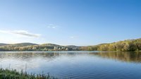 Tranquil lake surrounded by autumn forest hills under clear blue sky with calm water reflections creating peaceful natural landscape for relaxation and outdoor recreation.